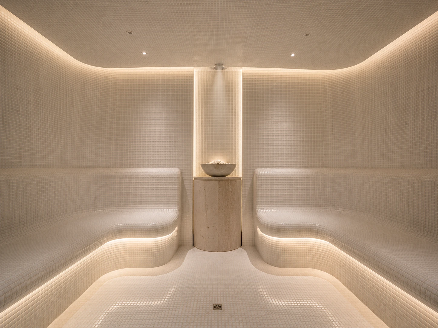 Light mosaic steam room with curved heated benches and concealed lighting