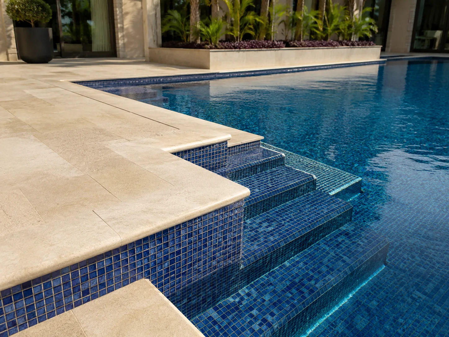 Close view of blue mosaic pool tiling, steps and stone coping